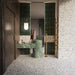 Bathroom featuring Stuzzi Lunar 60x60cm classical terrazzo style porcelain tiles with a 4D brushed finish, paired with deep green fluted wall tiles, green marble effect basins, brushed brass fittings and dark wood panelling for a luxurious contemporary interior.