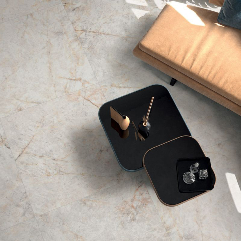 Living room featuring Taj Mahal Polished Marble effect 60 × 60cm porcelain wall and floor tiles, styled with soft neutral seating, black nesting tables, and warm natural light highlighting subtle veining.