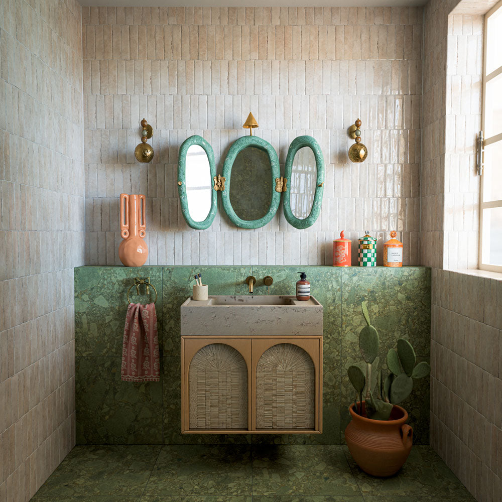 Bathroom featuring Terrazerri Terrazzo Green 60x60cm tiles, showcasing a rich green terrazzo effect surface with layered stone-inspired fragments and natural tonal variation. Used across the floor and lower walls, the large-format tiles create a seamless, luxurious look, while the soft neutral wall tiles, natural textures and decorative accents add warmth and contrast. The result is a bold yet elegant space inspired by Mediterranean design and contemporary interiors.