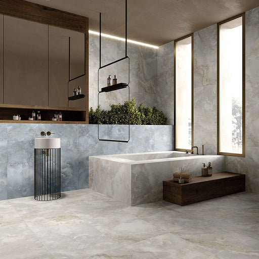 Contemporary luxury bathroom featuring Thebes Blue Honed Matt Onyx porcelain tiles on the walls and bath surround. The soft blue onyx-effect veining pairs beautifully with warm wood cabinetry, black accents and large-format stone effect floor tiles to create a calm, spa-inspired space.