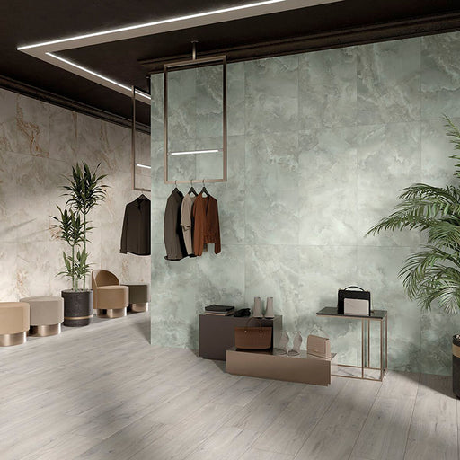 Contemporary retail interior featuring Thebes Green Honed Matt Onyx 60x120cm porcelain tiles on a large feature wall. The soft green onyx effect with flowing natural veining creates a luxurious backdrop, complemented by pale wood effect flooring, warm neutral furnishings and modern display fixtures.