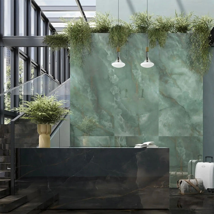 Modern commercial interior featuring Thebes Green Honed Matt Onyx porcelain tiles in a large-format feature wall. The soft green onyx-effect veining creates a striking focal point, complemented by black stone surfaces, hanging greenery and contemporary lighting for a luxurious reception space.