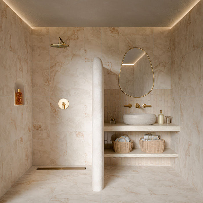 Luxury bathroom featuring Thebes Ivory honed matt onyx effect porcelain tiles in 60cm x 120cm. Large-format ivory marble effect wall and floor tiles with soft natural veining create a warm, spa-inspired bathroom, complemented by a cream brick tile splashback and elegant brass fixtures.