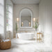 Elegant bathroom featuring Thebes White honed matt onyx effect porcelain wall and floor tiles in a 60cm x 60cm format, paired with a freestanding bath, classic wall panelling, an arched mirror, brushed brass fittings and soft neutral styling for a timeless luxury look.