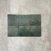 Flat lay of Zellige Royal Green Square 13.2 × 13.2cm Moroccan-style ceramic tiles in rich deep green tones, arranged in a simple grid on a textured grey background, showcasing the glossy glaze, natural tonal variation and handcrafted zellige-effect finish.