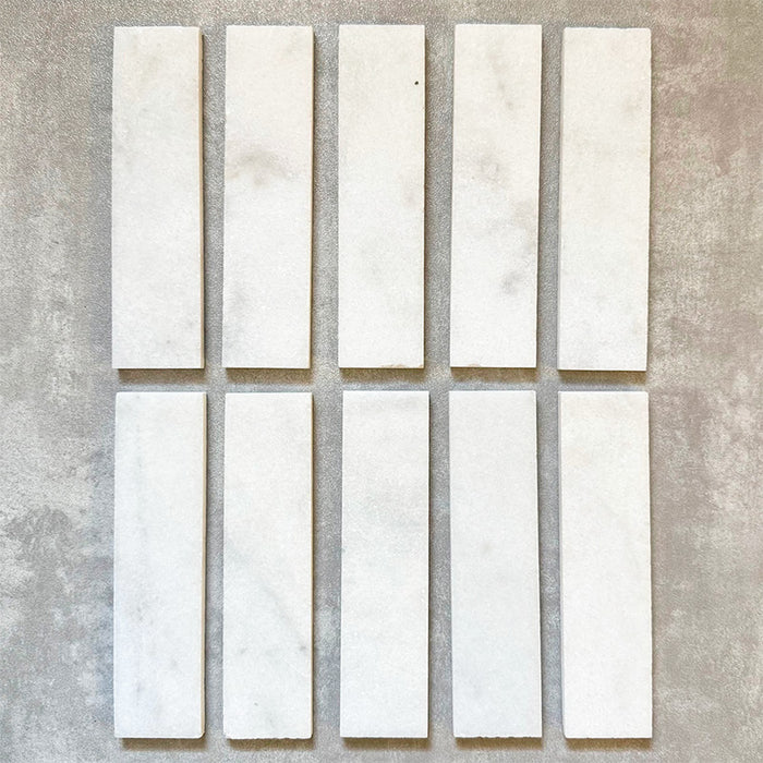 Fayrouz White 5x20cm natural marble tiles with a honed finish, featuring a soft white base with subtle grey veining, arranged in a neat grid to highlight natural variation and tonal consistency.