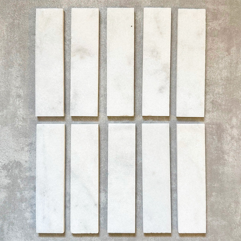 Fayrouz White 5x20cm natural marble tiles with a honed finish, featuring a soft white base with subtle grey veining, arranged in a neat grid to highlight natural variation and tonal consistency.