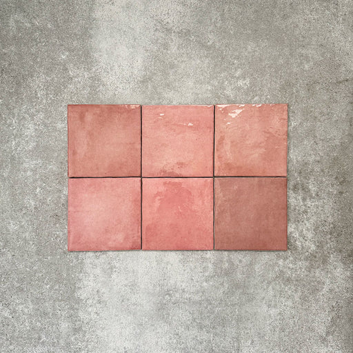 Flat lay of Zellige Rose Pink Square 13.2 × 13.2cm Moroccan-style ceramic tiles in soft blush, dusty rose and warm pink tones, showing subtle shade variation and gently uneven edges, arranged in a simple grid on a textured grey background to highlight the handcrafted zellige-effect surface.