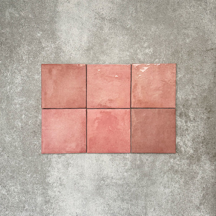 Flat lay of Zellige Rose Pink Square 13.2 × 13.2cm Moroccan-style ceramic tiles in soft blush, dusty rose and warm pink tones, showing subtle shade variation and gently uneven edges, arranged in a simple grid on a textured grey background to highlight the handcrafted zellige-effect surface.