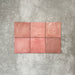 Flat lay of Zellige Rose Pink Square 13.2 × 13.2cm Moroccan-style ceramic tiles in soft blush, dusty rose and warm pink tones, showing subtle shade variation and gently uneven edges, arranged in a simple grid on a textured grey background to highlight the handcrafted zellige-effect surface.