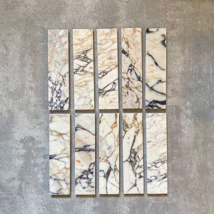 Set of Fayrouz Picasso 5x20cm natural marble tiles with a honed finish, displaying a white base with expressive grey, green and warm gold veining, showcasing natural tonal variation and unique patterning across individual pieces.