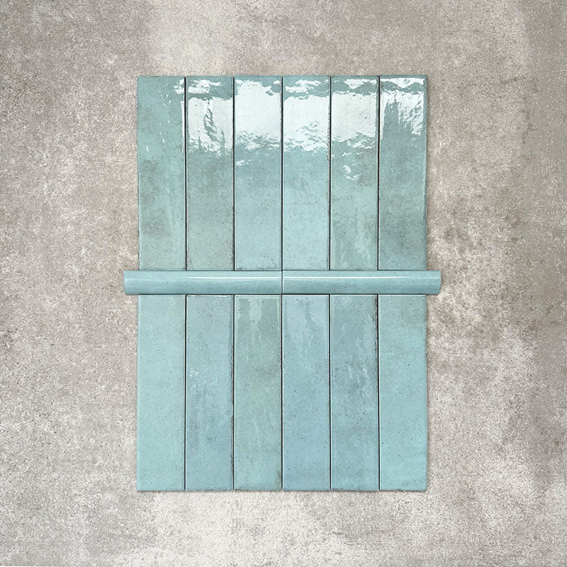 Nomad Aquamarine bullnose pencil border ceramic tiles in a 3 × 20cm format, shown alongside matching brick tiles, featuring a glossy finish and soft blue-green tones for a coordinated industrial-style wall detail.