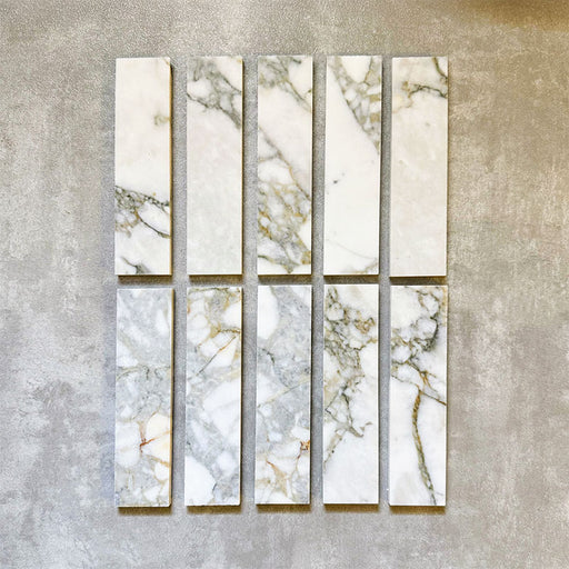 Arrangement featuring Fayrouz Calacatta Green 5x20cm natural marble tiles with a honed finish, displayed in a vertical layout to showcase soft white tones with green and gold veining against a neutral background.