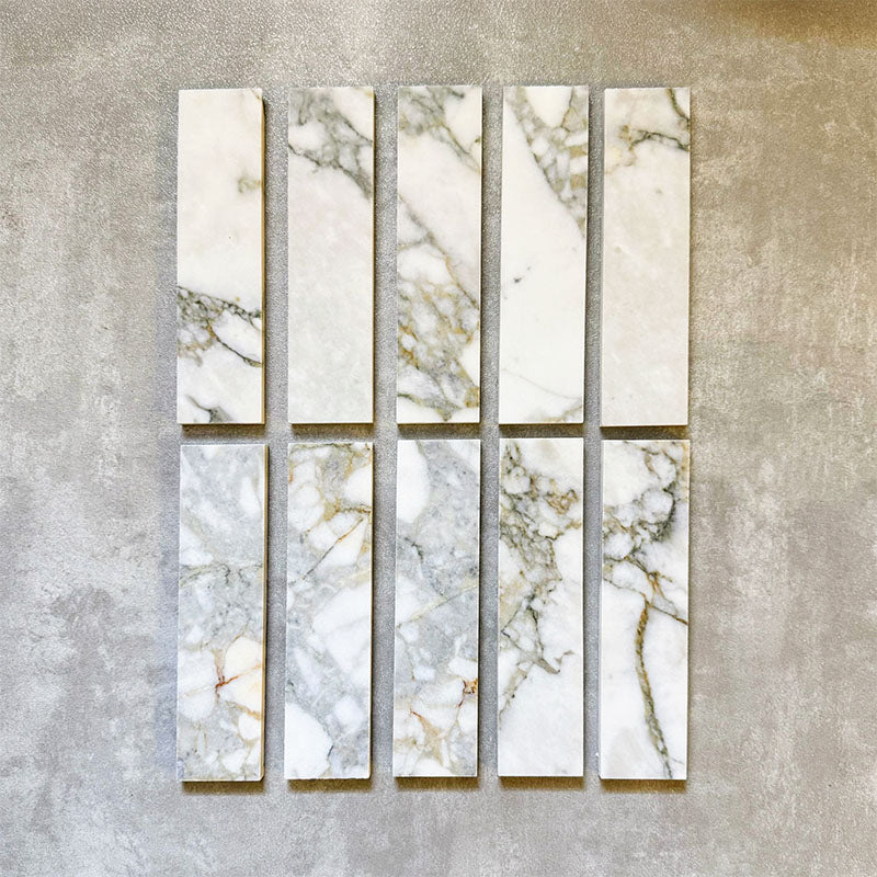 Arrangement featuring Fayrouz Calacatta Green 5x20cm natural marble tiles with a honed finish, displayed in a vertical layout to showcase soft white tones with green and gold veining against a neutral background.