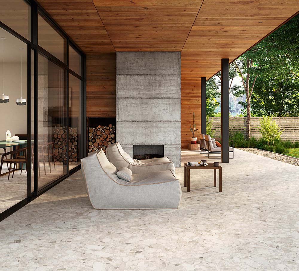Covered outdoor living area featuring Venice Ivory matt terrazzo effect 2cm porcelain paving in a 60 x 120cm format, creating a seamless anti-slip surface with contemporary architecture, timber ceilings and a modern fireplace.