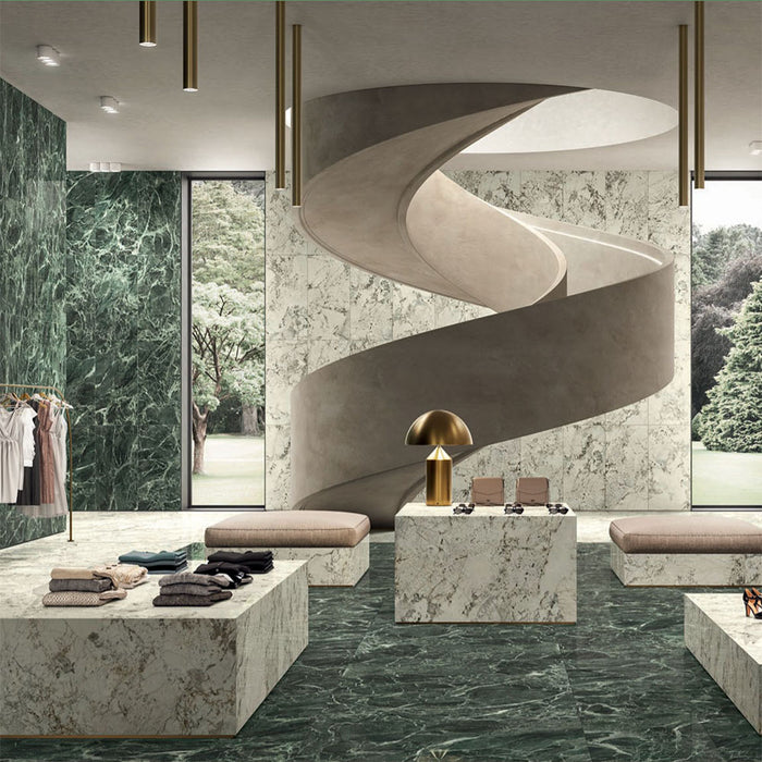 Retail interior featuring Verde Apia Polished Green Marble effect 60 × 60cm porcelain wall and floor tiles, styled with sculptural staircase, stone display plinths, and rich green tones with striking natural veining.