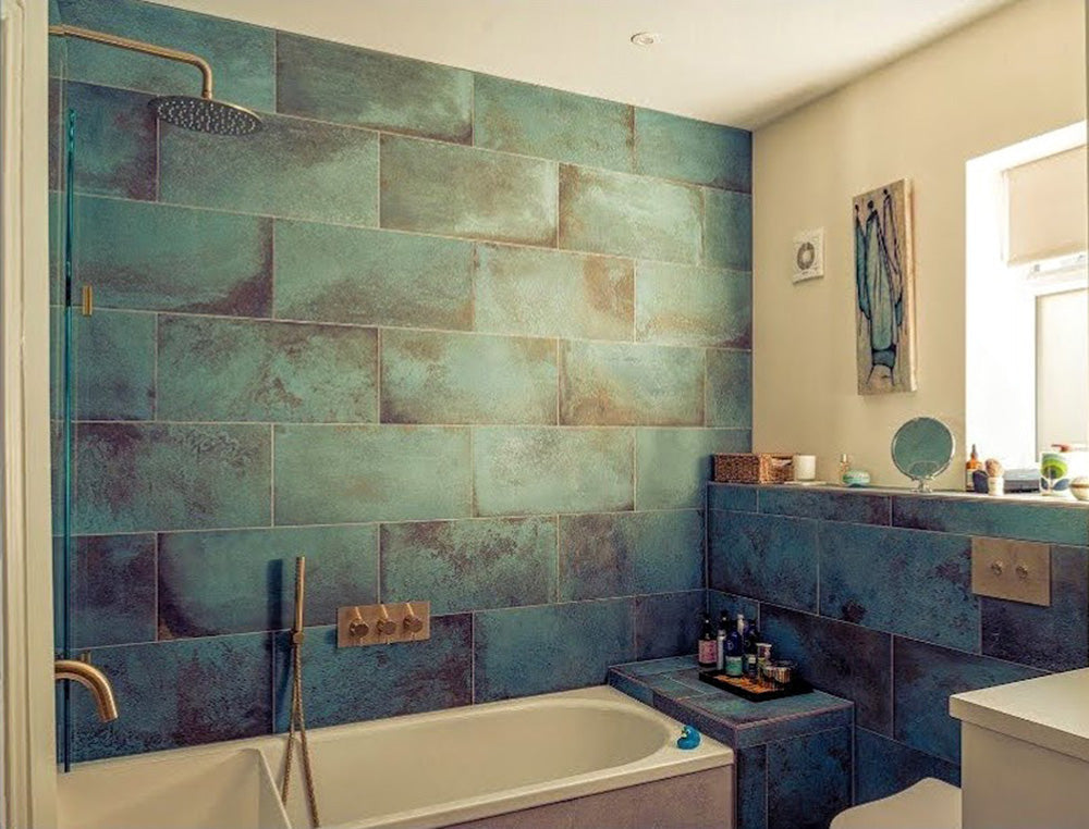 Contemporary bathroom featuring Verde Copper Oxide 30cm x 60cm metallic effect wall and floor tiles, styled with a built-in bath, brass shower fittings and rich blue-green tones for a luxurious interior.