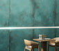 Contemporary dining area featuring Verde Copper Oxide 60cm x 60cm metallic effect wall tiles, paired with light wood furniture and subtle LED lighting to create a bold industrial-inspired feature wall.