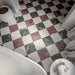 Bathroom floor featuring Divine Verde Green Matt Marble effect 30 × 30cm porcelain tiles in a chequerboard layout, combining green, red, and neutral tones, styled with soft furnishings and natural light.