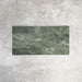 Arrangement featuring Fayrouz Verde 5x20cm natural marble tiles with a honed finish, laid in a horizontal brick pattern, showcasing rich green tones, natural veining and tonal variation against a neutral background.