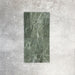 Fayrouz Verde 5x20cm natural marble tiles with a honed finish arranged vertically, showcasing rich green tones and natural veining, displayed against a neutral textured background in a clean product setting.