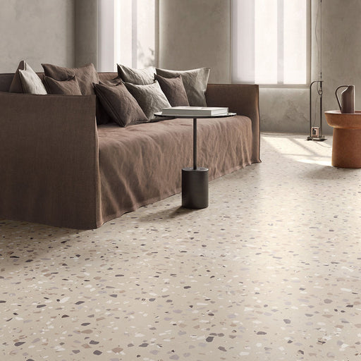 Contemporary living room featuring Verona Medium Sand concrete effect porcelain floor tiles with a terrazzo-inspired finish, complemented by a neutral linen sofa, warm earthy tones, minimalist furniture and soft natural light.