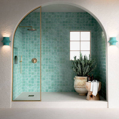 Verona Micro Sand 60cm x 60cm terrazzo concrete effect porcelain floor tiles, creating a soft neutral base in an arched walk-in shower with aqua green wall tiles, brass fittings and natural accents.