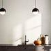 Contemporary kitchen featuring Verona Micro White concrete effect porcelain wall tiles, styled with dark cabinetry, black pendant lighting, warm wood accessories and minimalist décor for a bright, modern interior.