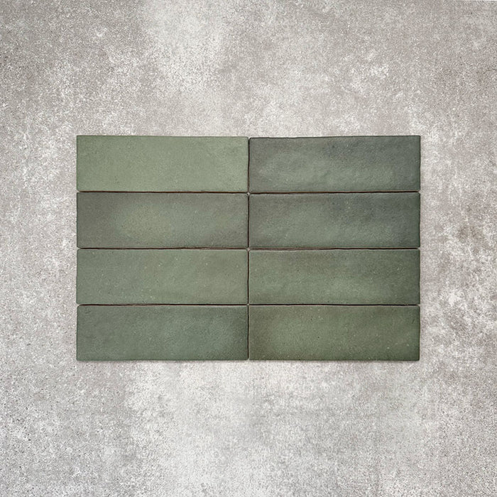 Flat lay of Zellige Malachite Green 6.5×20cm Moroccan-style ceramic brick tiles, showcasing subtle tonal variation, handmade-look texture and rich green glaze on a neutral background.