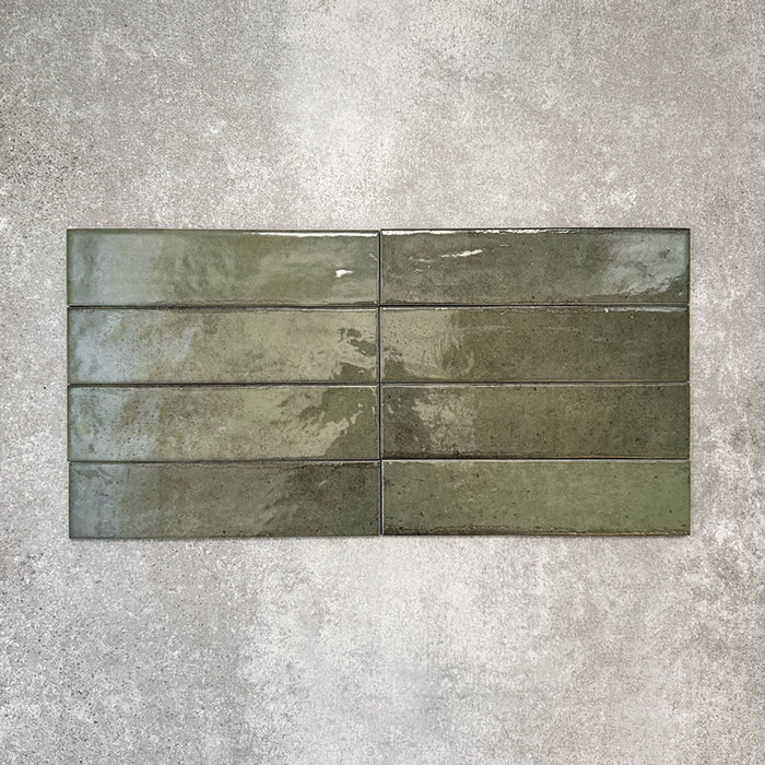 Nomad Sage Green brick wall tiles in a 6 × 24.6cm format, shown in a flat lay arrangement with a glossy, lightly textured surface and deep green tones, ideal for creating an industrial-style wall finish.