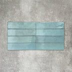 Nomad Aquamarine brick wall tiles in a 6 × 24.6cm format, shown laid vertically with a glossy, lightly textured surface and soft blue-green tones, creating an industrial-style look.