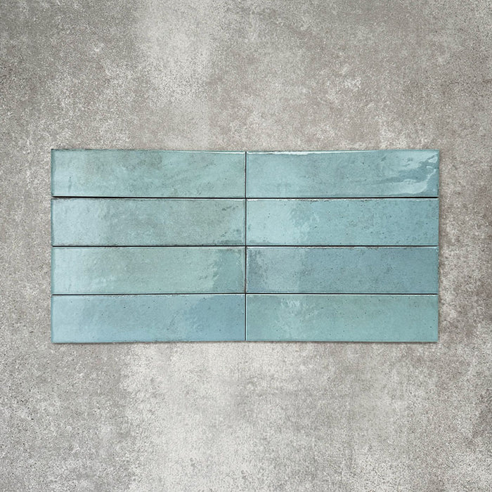 Nomad Aquamarine brick wall tiles in a 6 × 24.6cm format, shown laid vertically with a glossy, lightly textured surface and soft blue-green tones, creating an industrial-style look.