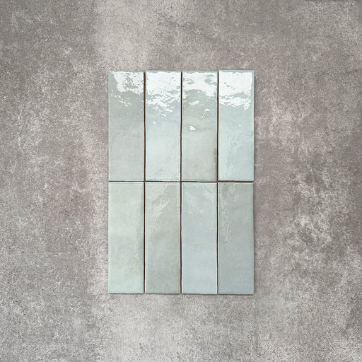 Flat lay of Zellige Aqua 6.5×20cm Moroccan-style ceramic brick tiles, showcasing soft blue-green tones, a glossy handmade-look glaze and subtle tonal variation on a neutral background.