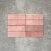 Flat lay of Zellige Rose Pink Brick 6.5 × 20cm Moroccan-style ceramic tiles, shown in soft blush, dusty rose and terracotta pink tones with gentle tonal variation and lightly uneven edges, arranged in a vertical brick layout on a textured grey background to showcase the handcrafted zellige-effect glaze.