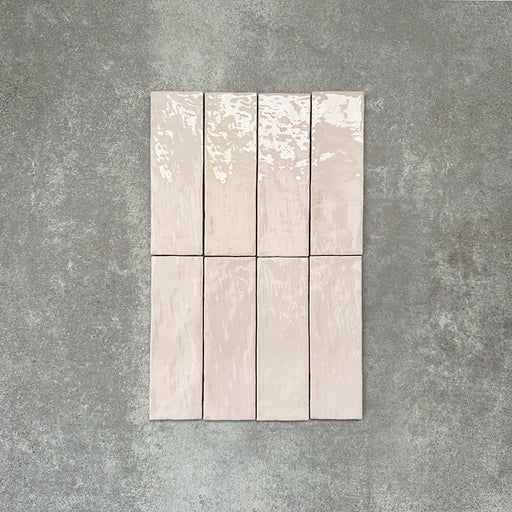 Flat lay of Zellige Pink Mist Brick 6.5 × 20cm Moroccan-style ceramic tiles in soft pale pink and blush tones, arranged in a vertical brick layout on a textured grey background, showcasing the glossy glaze, gentle tonal variation and handcrafted zellige-effect finish.