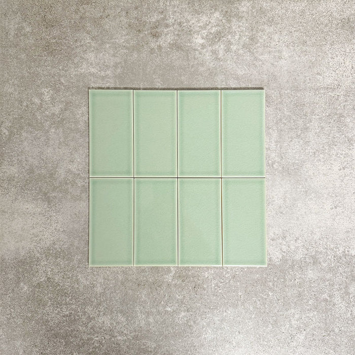 Close-up of Pimlico Lime Green 7.5 × 15cm ceramic tiles with a crackle glaze finish, showcasing soft green tones, subtle surface texture and a smooth rectangular format ideal for bathroom and kitchen walls.