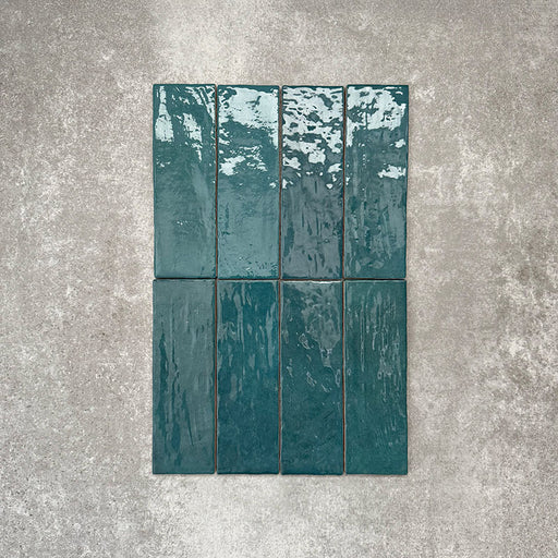 Flat lay of Zellige Peacock Green 6.5×20cm Moroccan-style ceramic brick tiles, showcasing deep blue-green tones, a glossy handmade-look glaze and natural tonal variation on a neutral background.