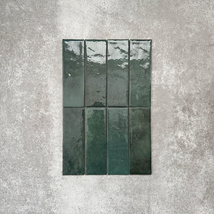 Flat lay of Zellige Royal Green Brick 6.5 × 20cm Moroccan-style ceramic tiles in rich deep green tones, arranged in a vertical brick layout on a textured grey background, showcasing the glossy glaze, natural tonal variation and handcrafted zellige-effect finish.