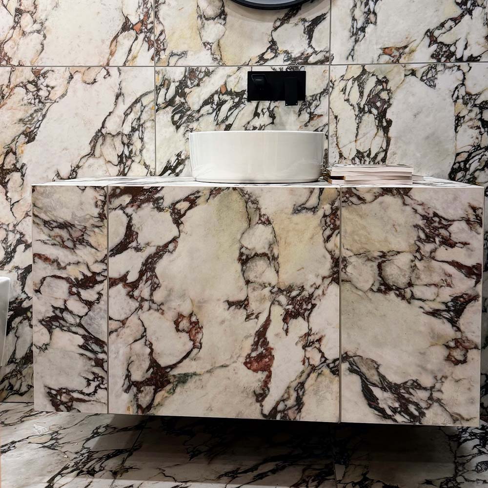 Bathroom vanity area featuring Viola Matt Honed Marble effect 60 × 60cm porcelain wall and floor tiles, styled with a floating basin, black wall-mounted tap, and bold veining in cream, burgundy, and charcoal tones.