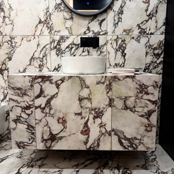 Bathroom vanity area featuring Viola Matt Honed Marble effect 60 × 60cm porcelain wall and floor tiles, styled with a floating basin, black wall-mounted tap, and bold veining in cream, burgundy, and charcoal tones.