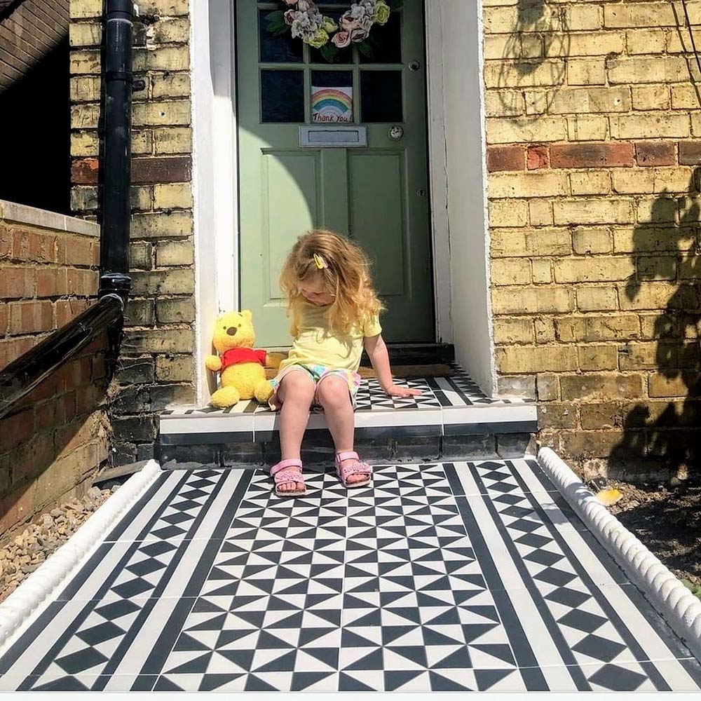 Front garden walkway featuring Fulham Tile Black & White Victorian-style porcelain wall and floor tiles in a 25 × 25cm format, laid in a bold geometric pattern with a contrasting border, creating a striking entrance to a period brick home with a painted front door.