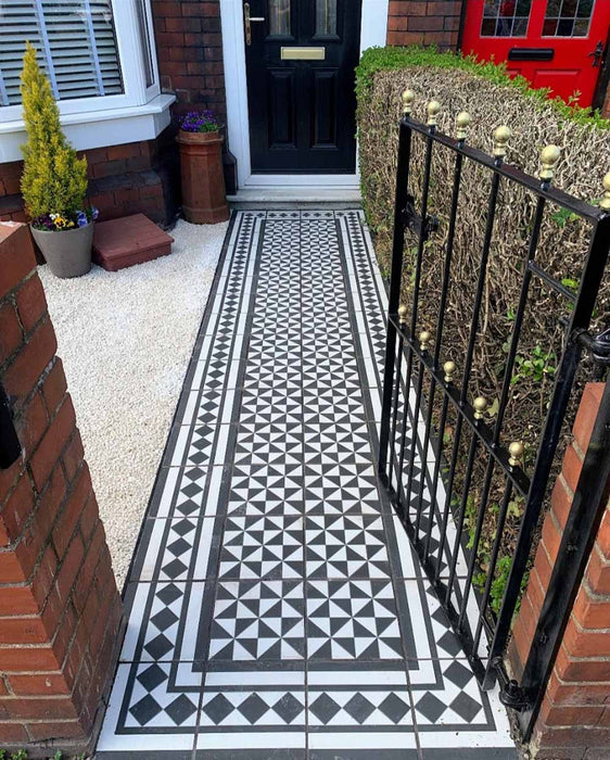 Front garden walkway featuring Fulham Tile Black & White Victorian-style porcelain wall and floor tiles in a 25 × 25cm format, laid in a classic geometric pattern with a framed border, creating a striking path to a traditional brick house with wrought iron gates.