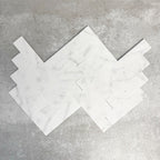 Arrangement featuring Fayrouz White 5x20cm natural marble tiles with a honed finish, laid in a herringbone pattern to create directional movement, showcasing a soft white base with subtle grey veining and gentle tonal variation.