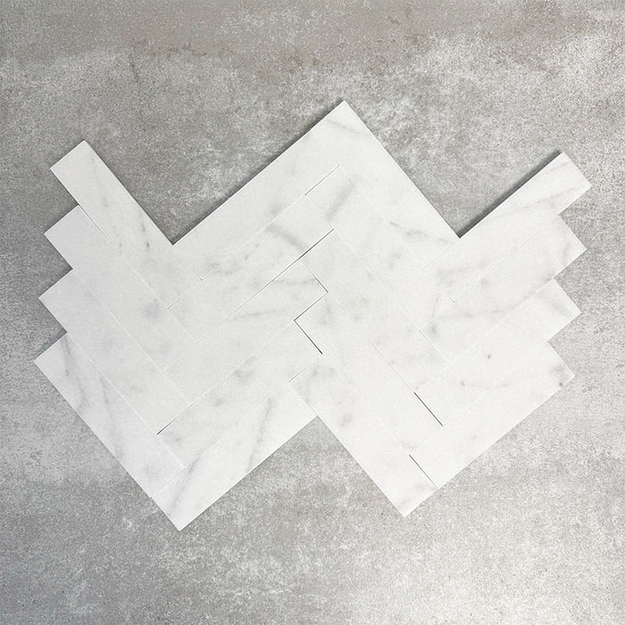 Arrangement featuring Fayrouz White 5x20cm natural marble tiles with a honed finish, laid in a herringbone pattern to create directional movement, showcasing a soft white base with subtle grey veining and gentle tonal variation.
