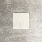 Single Fayrouz White 15.2x15.2cm natural marble tile with a honed finish, featuring soft white tones and subtle natural markings, displayed against a neutral textured background in a clean product setting.