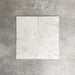 Four Fayrouz White 15.2x15.2cm natural marble tiles with a honed finish arranged together, showcasing soft white tones, subtle markings and natural variation against a neutral textured background.