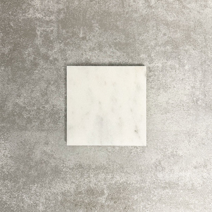 Single Fayrouz White 15.2x15.2cm natural marble tile with a honed finish, featuring soft white tones and subtle natural markings, displayed against a neutral textured background in a clean product setting.