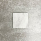 Single Fayrouz White 15.2x15.2cm natural marble tile with a tumbled finish, featuring soft white tones and subtle natural veining, displayed against a neutral textured background in a clean product setting.