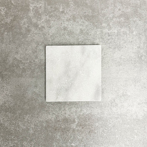 Single Fayrouz White 15.2x15.2cm natural marble tile with a tumbled finish, featuring soft white tones and subtle natural veining, displayed against a neutral textured background in a clean product setting.
