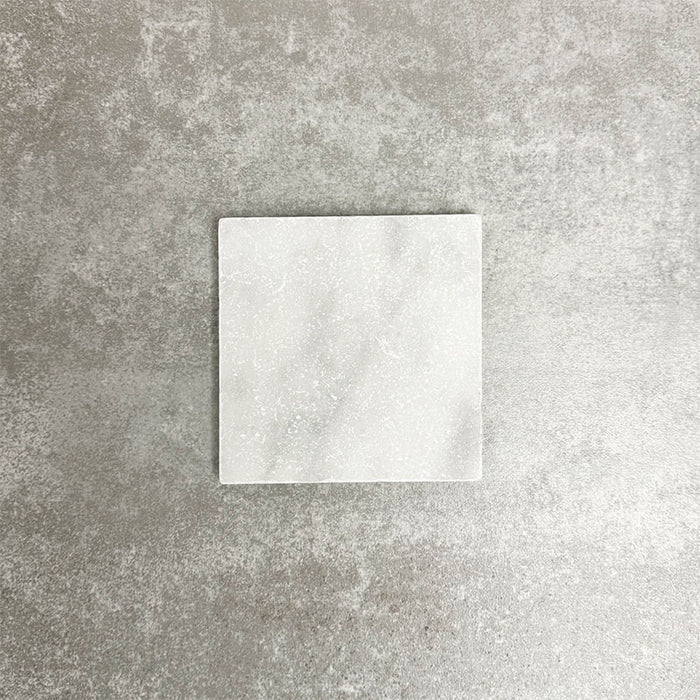 Single Fayrouz White 15.2x15.2cm natural marble tile with a tumbled finish, featuring soft white tones and subtle natural veining, displayed against a neutral textured background in a clean product setting.